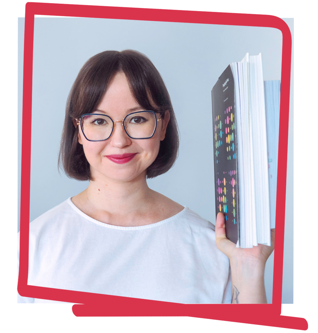Profile photo of Marta Dec, book designer, in a white shirt, on a light background, holding up a book.